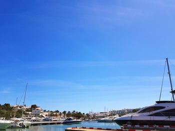 Sailboats moored at harbor against blue sky