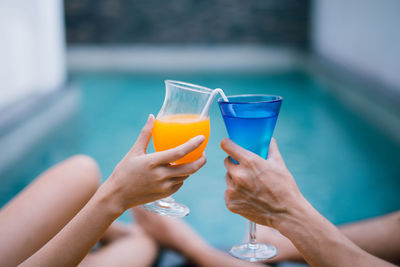 Close-up of hand holding drink against blue water