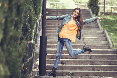 Portrait of young woman holding column while standing on steps