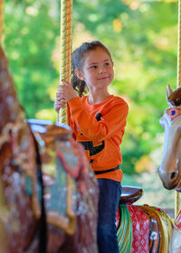 Pretty girl in a halloween themed shirt is riding a carousel at the carnival