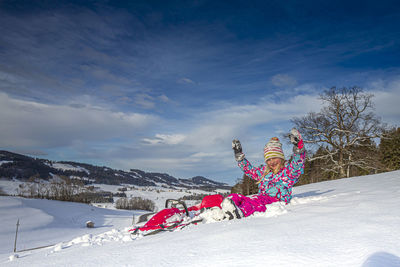 Full length portrait of girl sitting on snow covered land during winter