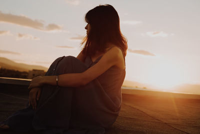 Mature woman sitting on terrace against sky during sunset