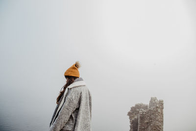 Side view of lady in warm clothes with open arms walking in foggy park on cloudy day