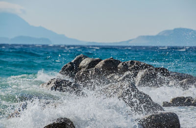 Sea waves splashing on rocks against sky