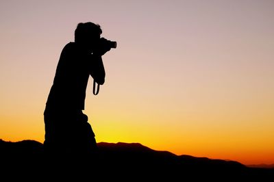 Silhouette man photographing against sky during sunset