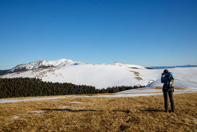 Rear view of man standing on snowcapped mountain against clear sky