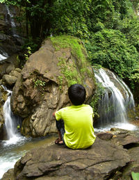 Rear view of boy looking at waterfall in forest