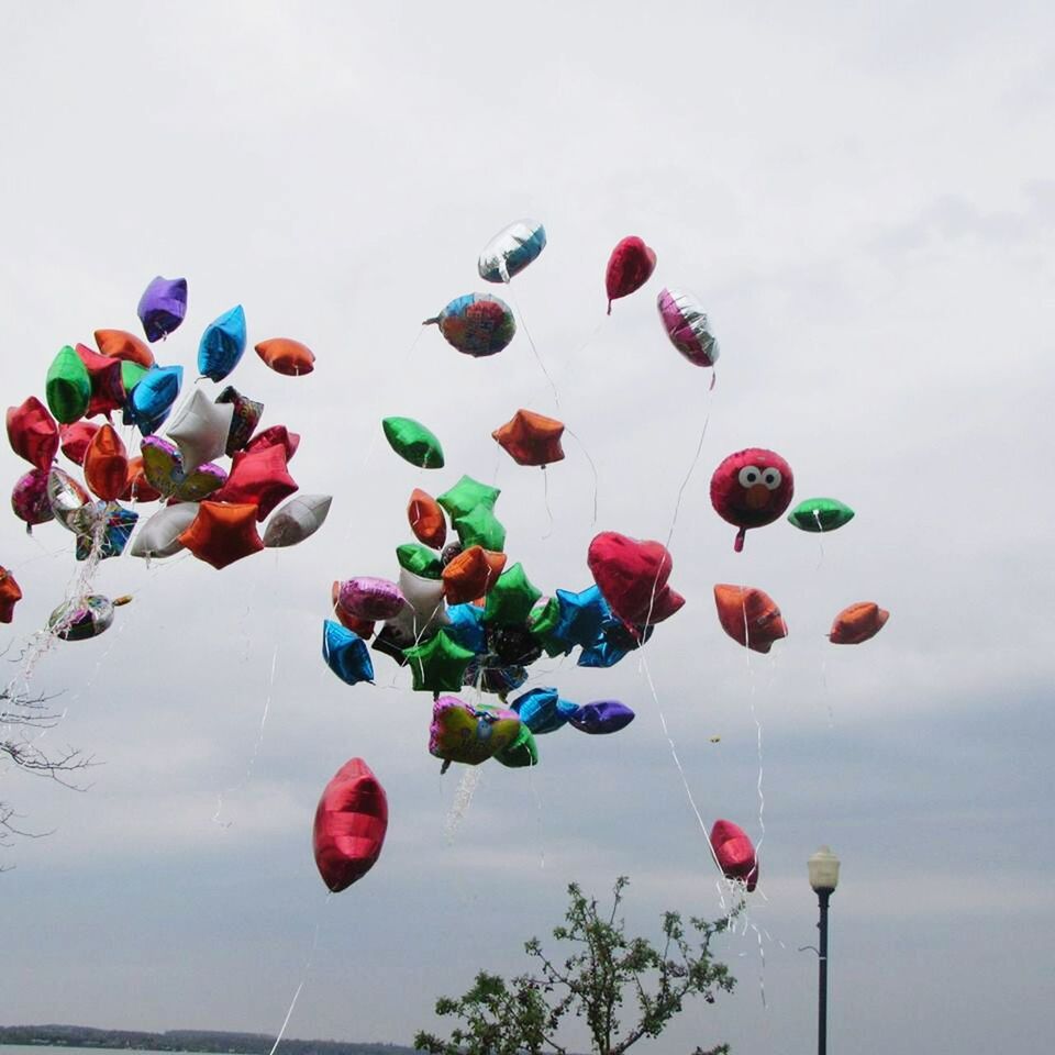 multi colored, low angle view, sky, mid-air, balloon, flying, colorful, variation, cloud - sky, day, no people, outdoors, nature, in a row, celebration, large group of objects, blue, reflection, hot air balloon, beauty in nature