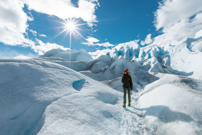 Woman walking on snow covered mountain against sky