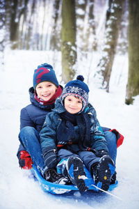 Portrait of siblings tobogganing on snow covered land