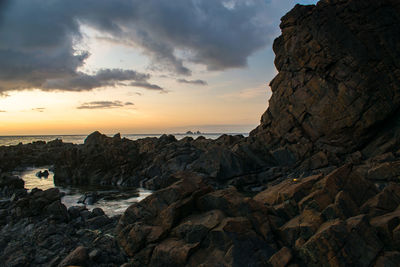 Rock formation on beach against sky during sunset