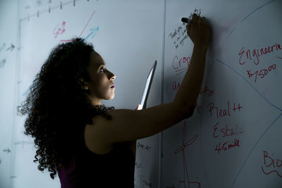 Businesswoman writing on whiteboard over tablet computer in office