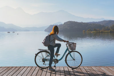 Rear view of woman with bicycle by lake