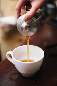 Cropped hand of woman pouring coffee in cup on table