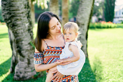 Mother and daughter standing against tree