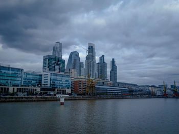 Modern buildings by river against sky in city