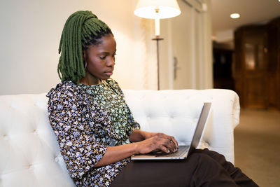 Young african american female freelancer typing on modern netbook while working remotely in living room at home