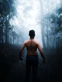 Rear view of shirtless man standing in forest