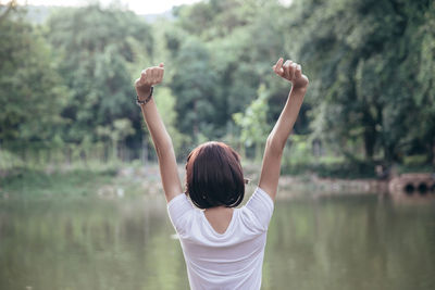 Rear view of woman with arms raised standing by lake