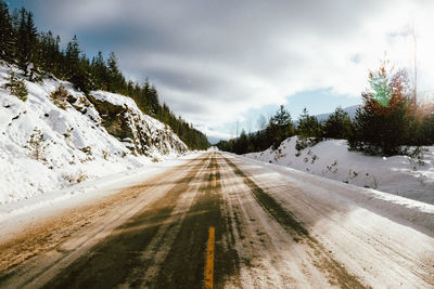 Road amidst trees against sky during winter