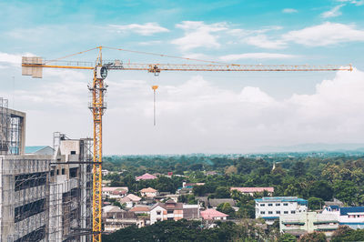 Cranes and buildings in city against sky