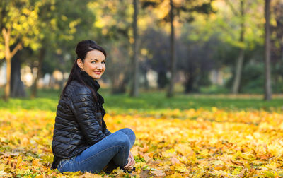 Portrait of smiling young woman sitting on autumn leaves