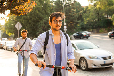 Portrait of young man riding push scooter on street