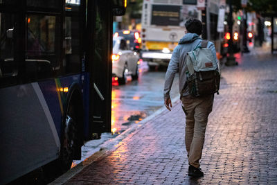 Rear view of man walking on wet street at night