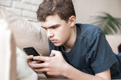 Teenage boy using smart phone lying on sofa at home