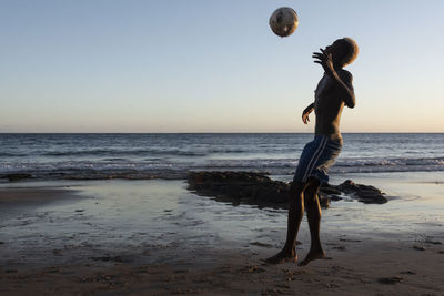 Man playing with ball on beach against clear sky