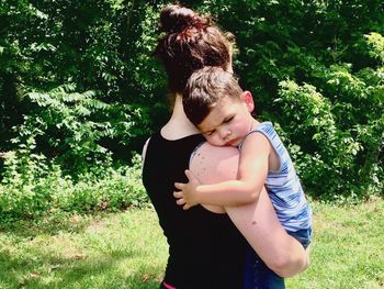 Rear view of mother carrying baby boy against trees at park