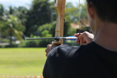 Rear view of man holding bow and arrow on field