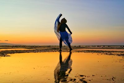 Full length of woman dancing at beach against clear sky during sunset