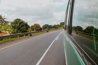 View of bus windows and trees by the  road against sky