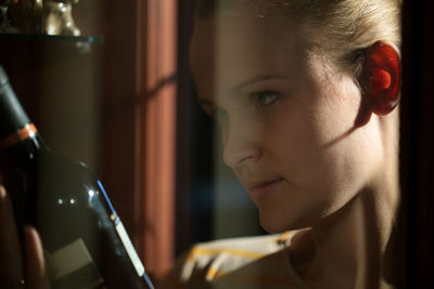 Close-up of young woman looking at wine bottle seen through glass