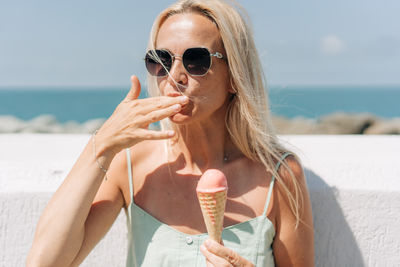 Cheerful carefree woman eats melting ice cream on the seashore on a hot summer day.