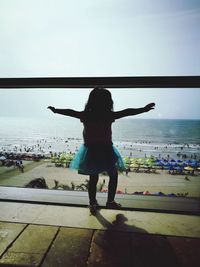 Rear view of woman with arms outstretched against sea