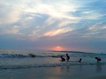 Children enjoying at beach against sky during sunset