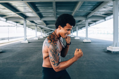 Shirtless male boxer practicing below bridge