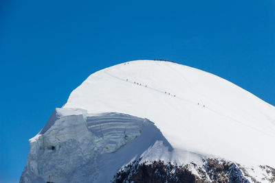 Low angle view of snowcapped mountain against clear blue sky