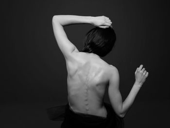 Rear view of shirtless woman against black background