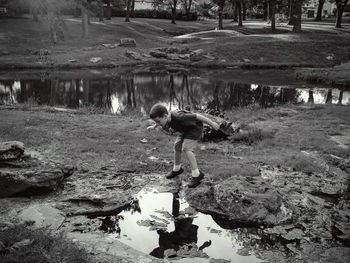 Full length of boy looking at puddle near pond against trees in park