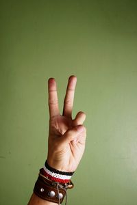 Cropped hand of man showing peace sign against green wall