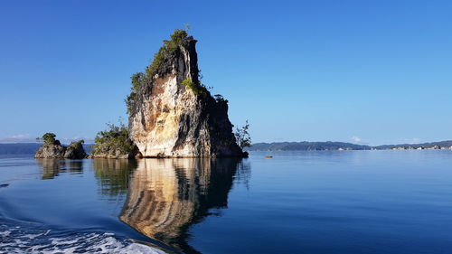 Rock formation in sea against clear blue sky