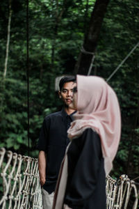 Portrait of young man with girlfriend standing on footbridge in forest