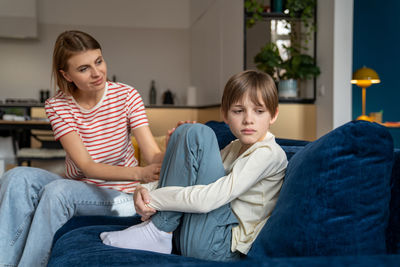 Portrait of siblings sitting on sofa at home