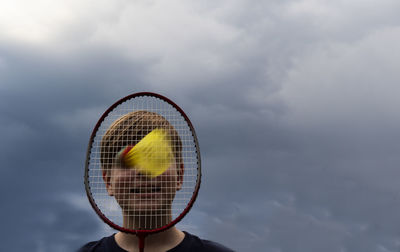 Close-up of boy playing badminton against sky