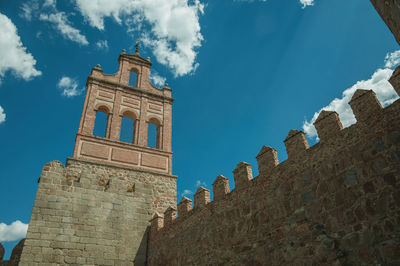 Stone city wall with merlons and tower made by bricks with iron wind vane, in avila,spain.