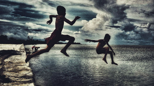 Men jumping on beach against sky