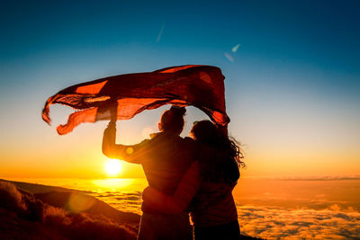 Couple holding scarf while looking at view against orange sunset sky